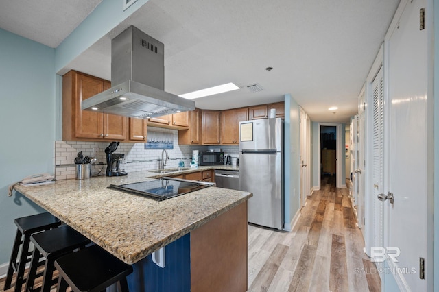 517 E Beach Blvd Unit 1B, Gulf Shores, AL 36542 - kitchen featuring appliances with stainless steel finishes, island exhaust hood, a sink, a peninsula, and light wood finished floors