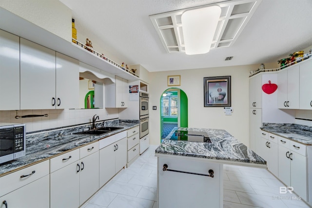 kitchen with dark stone countertops, appliances with stainless steel finishes, tasteful backsplash, and white cabinets