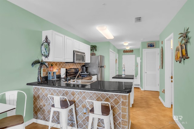 kitchen with appliances with stainless steel finishes, kitchen peninsula, white cabinetry, and a breakfast bar