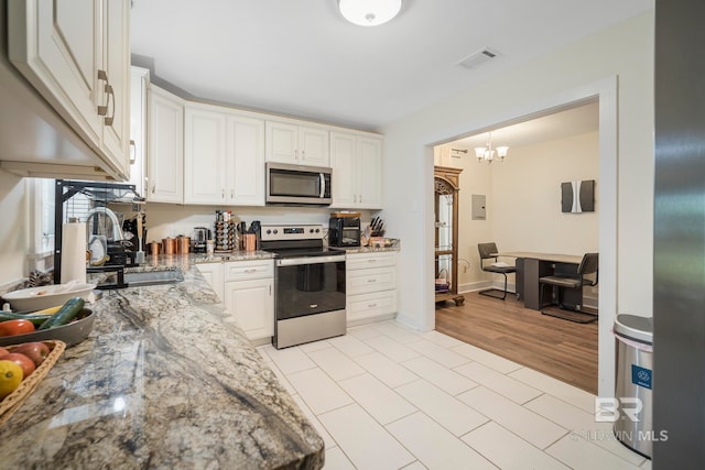 kitchen featuring stainless steel appliances, light stone countertops, a chandelier, white cabinets, and light hardwood / wood-style floors