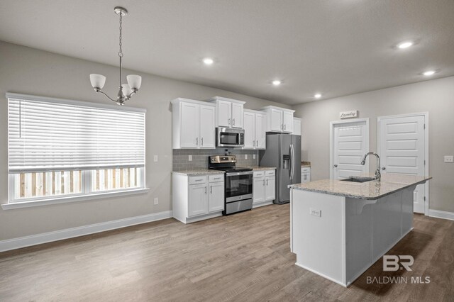 kitchen featuring appliances with stainless steel finishes, light hardwood / wood-style flooring, light stone countertops, tasteful backsplash, and white cabinetry