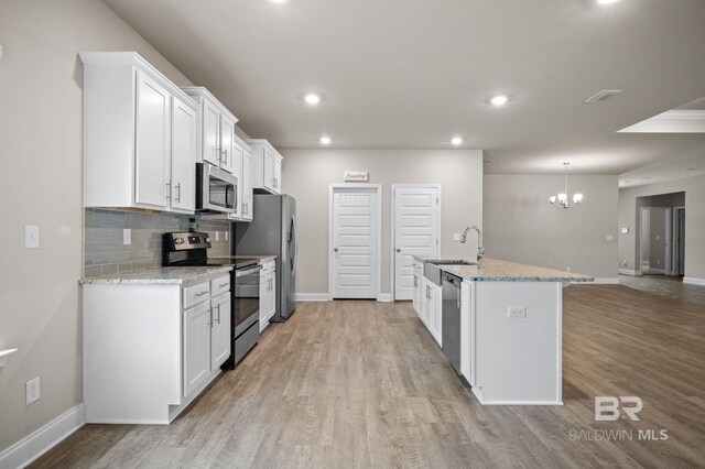 kitchen with stainless steel appliances, light hardwood / wood-style flooring, a center island with sink, light stone countertops, and white cabinets