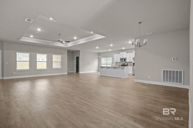 unfurnished living room featuring hardwood / wood-style floors, a wealth of natural light, ceiling fan, and a tray ceiling