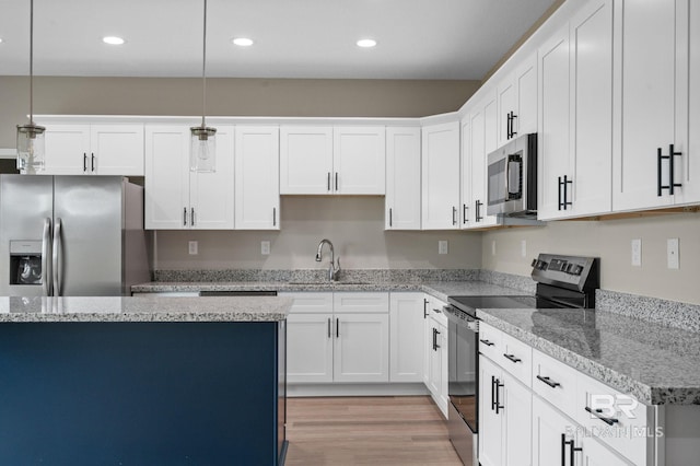 kitchen with stainless steel appliances, light wood-type flooring, decorative light fixtures, sink, and white cabinets