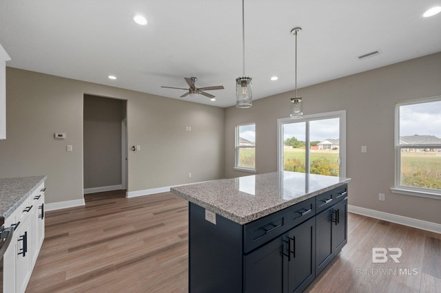 kitchen with light stone counters, hanging light fixtures, light hardwood / wood-style floors, white cabinets, and ceiling fan