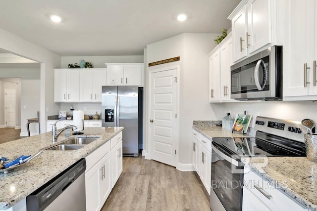 kitchen with appliances with stainless steel finishes, light wood-type flooring, a sink, and white cabinets