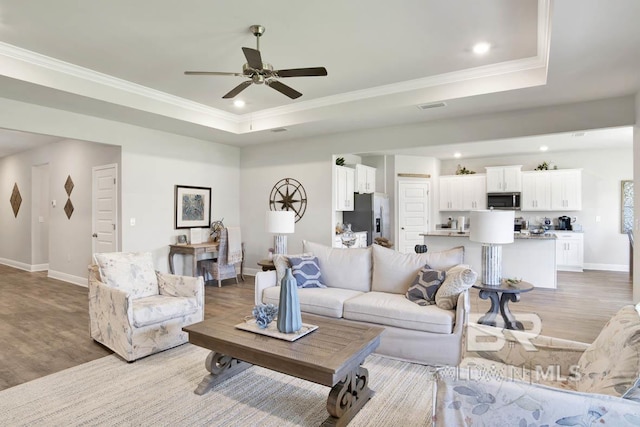 living area with light wood finished floors, baseboards, a raised ceiling, crown molding, and recessed lighting