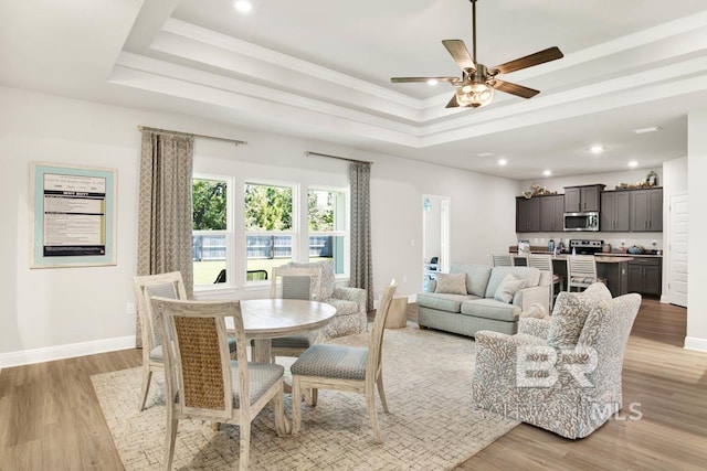 living room with crown molding, light wood finished floors, a raised ceiling, a ceiling fan, and baseboards