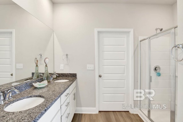 bathroom with double vanity, wood finished floors, a sink, and a shower stall