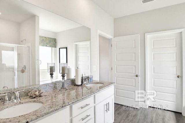 full bath featuring double vanity, wood finished floors, a sink, and a shower stall