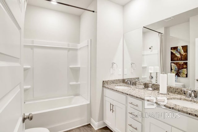 full bath with toilet, double vanity, tub / shower combination, and a sink