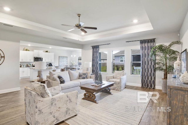 living room featuring ornamental molding, light wood-type flooring, a raised ceiling, and visible vents