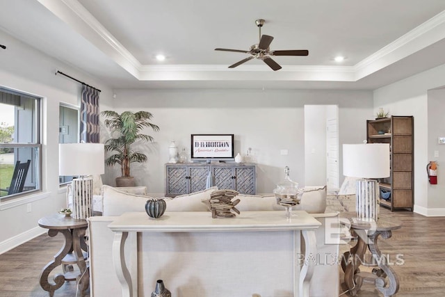 living room with a raised ceiling, crown molding, baseboards, and wood finished floors