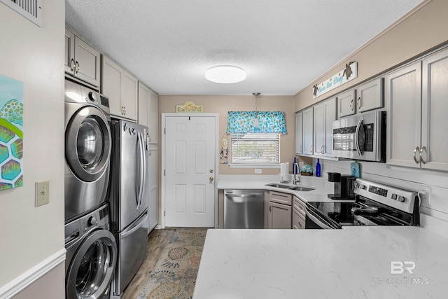 728 W Beach Blvd Unit 104, Gulf Shores, AL 36542 - kitchen with appliances with stainless steel finishes, a sink, a textured ceiling, stacked washing maching and dryer, and gray cabinets