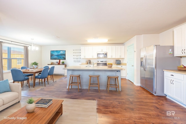 kitchen with hanging light fixtures, hardwood / wood-style flooring, appliances with stainless steel finishes, white cabinetry, and a breakfast bar area