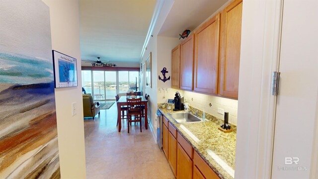 kitchen featuring decorative backsplash, light stone countertops, ceiling fan, stainless steel dishwasher, and sink