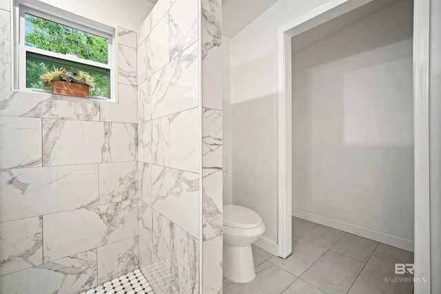 bathroom with tiled shower, toilet, and baseboards