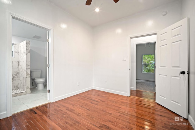 unfurnished bedroom with visible vents, a ceiling fan, ensuite bath, wood finished floors, and baseboards