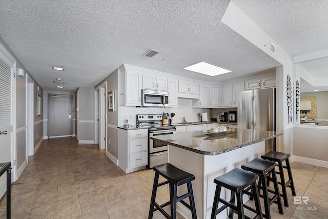 kitchen featuring white cabinets, a kitchen breakfast bar, dark stone counters, a center island, and stainless steel appliances