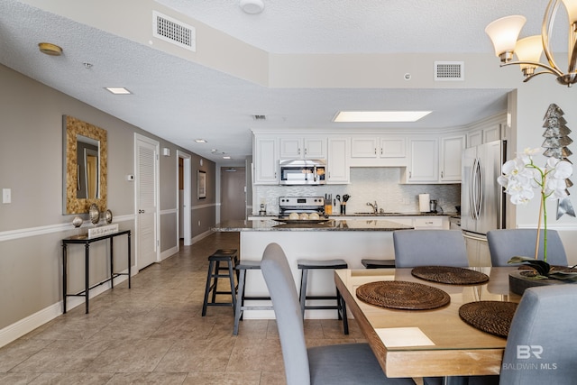 kitchen featuring sink, a breakfast bar area, dark stone countertops, white cabinetry, and stainless steel appliances