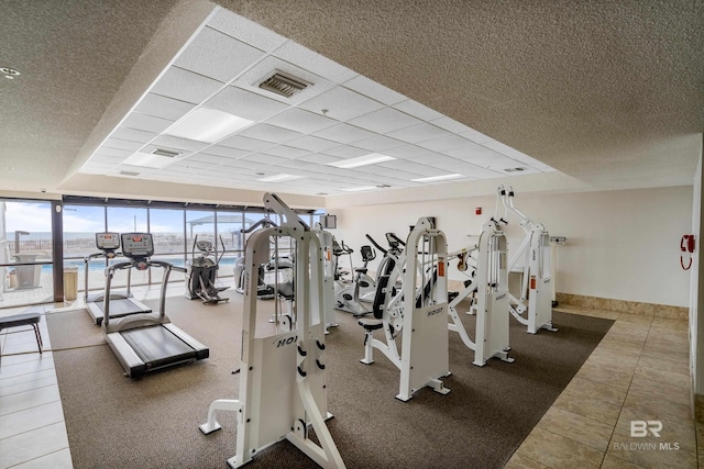 gym featuring a paneled ceiling, tile patterned floors, a wall of windows, and a water view