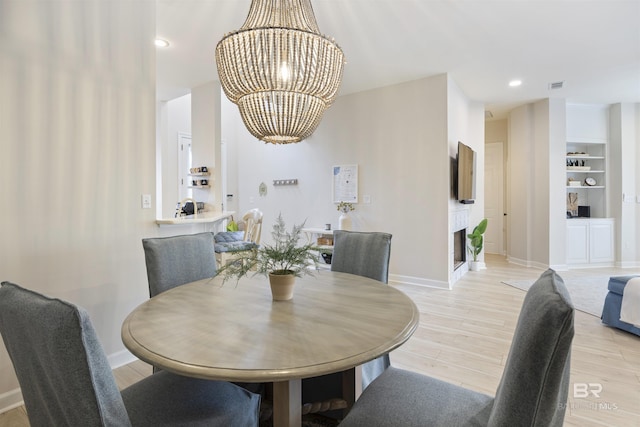 dining space featuring light wood-style floors, built in shelves, and an inviting chandelier