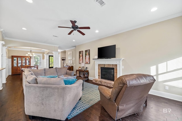 living room with ceiling fan with notable chandelier, ornamental molding, a fireplace, ornate columns, and dark hardwood / wood-style flooring