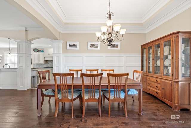 dining space featuring dark wood-type flooring, crown molding, a notable chandelier, and ornate columns