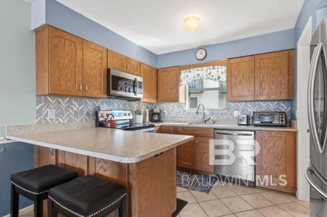 kitchen with a breakfast bar, sink, kitchen peninsula, stainless steel appliances, and decorative backsplash