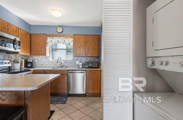 kitchen with sink, light tile patterned floors, stainless steel appliances, stacked washer and clothes dryer, and kitchen peninsula