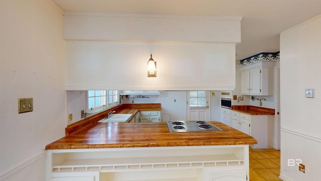 kitchen with stainless steel cooktop, a peninsula, a sink, and white cabinetry