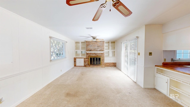 unfurnished living room with built in features, visible vents, a ceiling fan, a brick fireplace, and light carpet