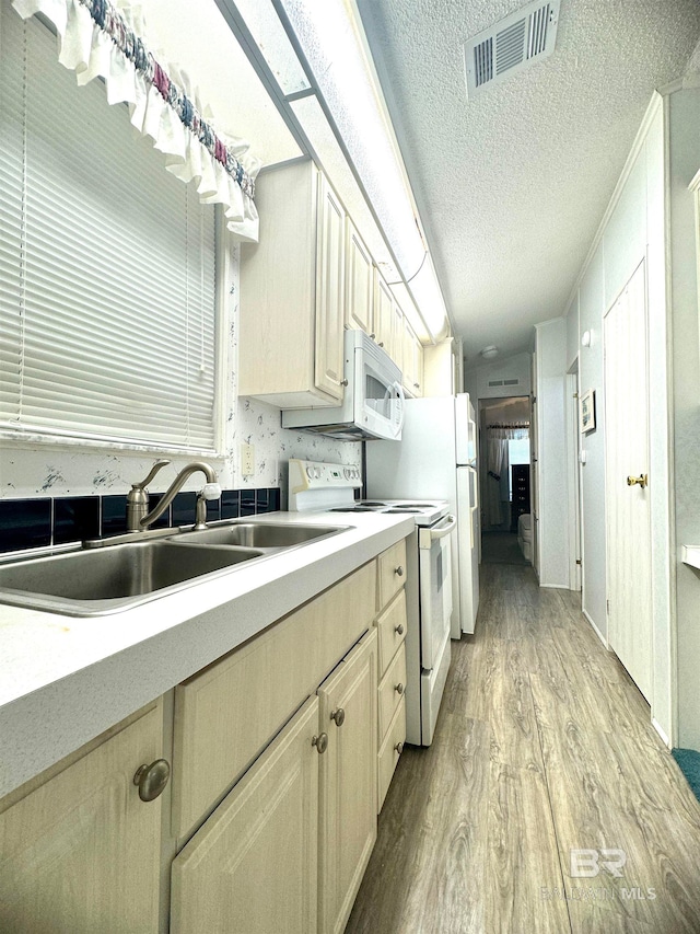 kitchen with a sink, white appliances, light countertops, light wood-type flooring, and visible vents