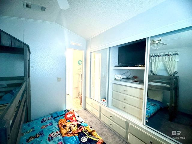 carpeted bedroom featuring ceiling fan, visible vents, a textured ceiling, vaulted ceiling, and a closet