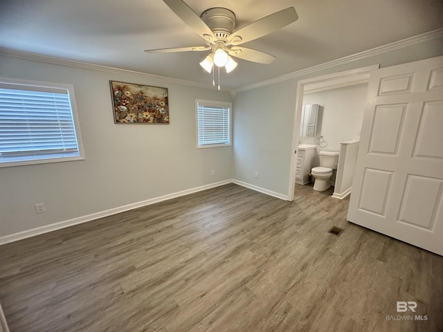 unfurnished bedroom with crown molding, visible vents, wood finished floors, baseboards, and ensuite bathroom
