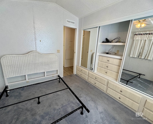 bedroom with a textured ceiling, visible vents, vaulted ceiling, a closet, and carpet flooring