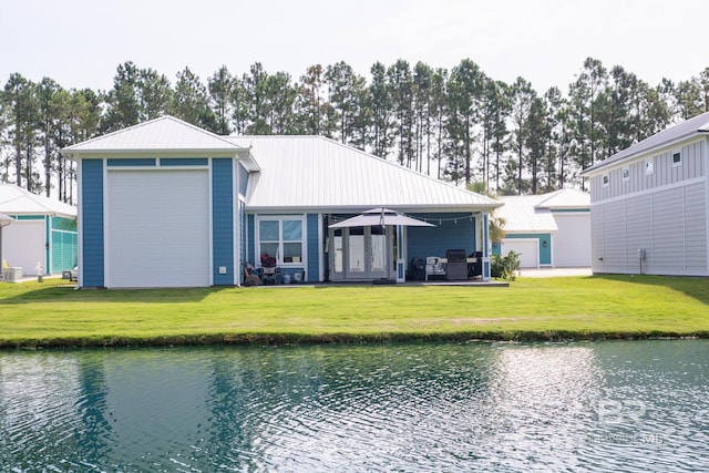 back of property with a garage, a water view, and a lawn