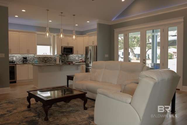 living room with lofted ceiling, ornamental molding, light wood-type flooring, and beverage cooler