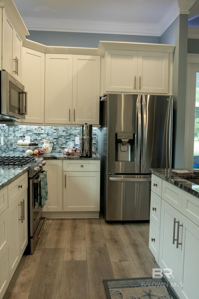 kitchen with backsplash, dark stone countertops, ornamental molding, light wood-type flooring, and appliances with stainless steel finishes