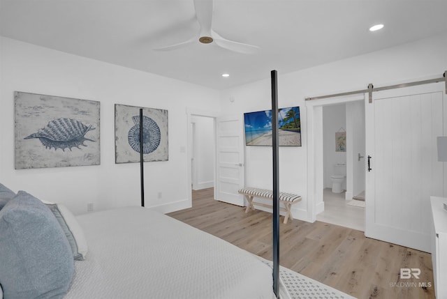 bedroom featuring ceiling fan, a barn door, recessed lighting, wood finished floors, and ensuite bath