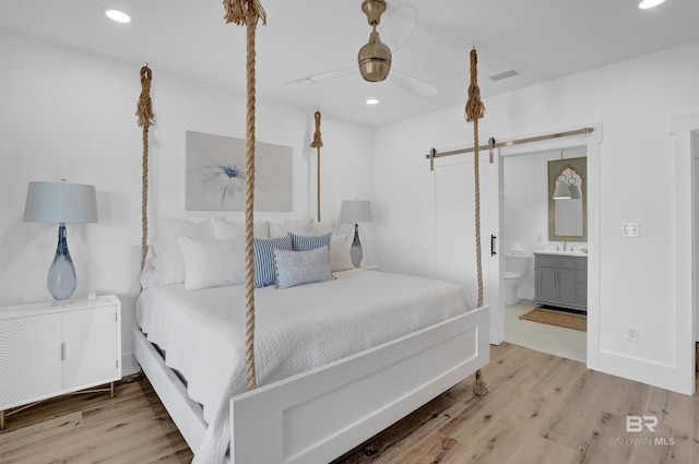 bedroom with connected bathroom, radiator, a barn door, wood finished floors, and a sink