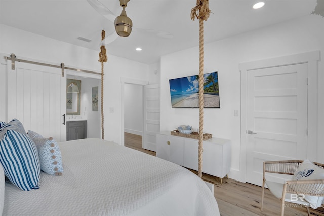 bedroom featuring recessed lighting, a barn door, visible vents, and wood finished floors