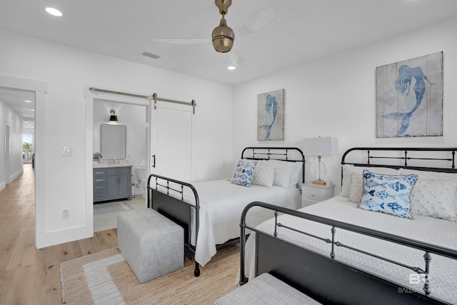 bedroom with visible vents, light wood-type flooring, a barn door, recessed lighting, and ensuite bath