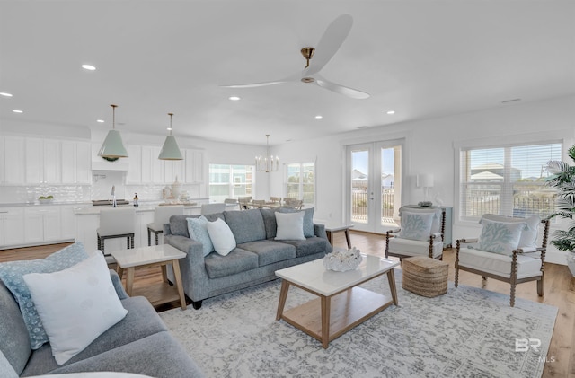 living room with ceiling fan with notable chandelier, recessed lighting, french doors, and light wood finished floors