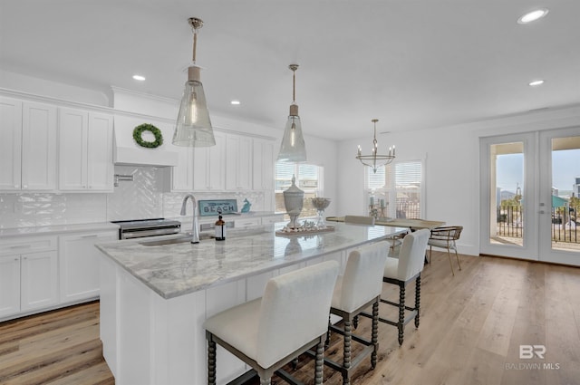 kitchen with light stone counters, decorative backsplash, light wood-style flooring, white cabinets, and a sink