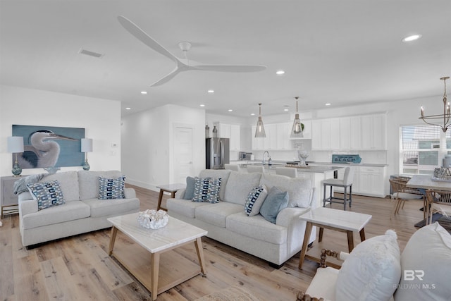 living area featuring visible vents, recessed lighting, ceiling fan with notable chandelier, and light wood-style flooring