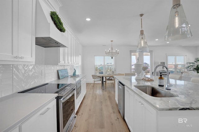 kitchen featuring light wood-type flooring, a sink, white cabinetry, appliances with stainless steel finishes, and wall chimney range hood