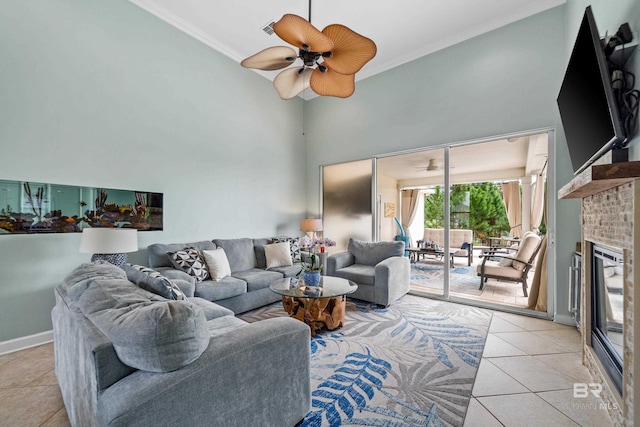 living room featuring light tile patterned floors, a ceiling fan, a high ceiling, crown molding, and a brick fireplace