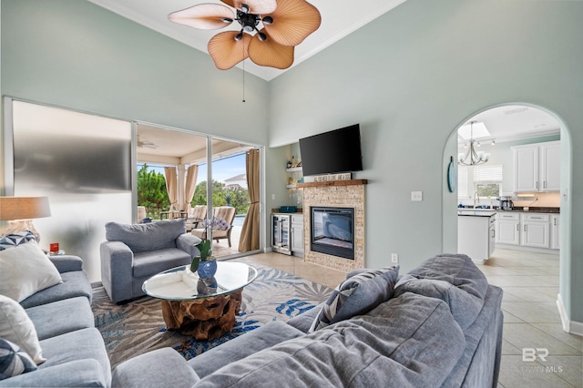 living area featuring crown molding, a towering ceiling, a ceiling fan, a glass covered fireplace, and light tile patterned flooring