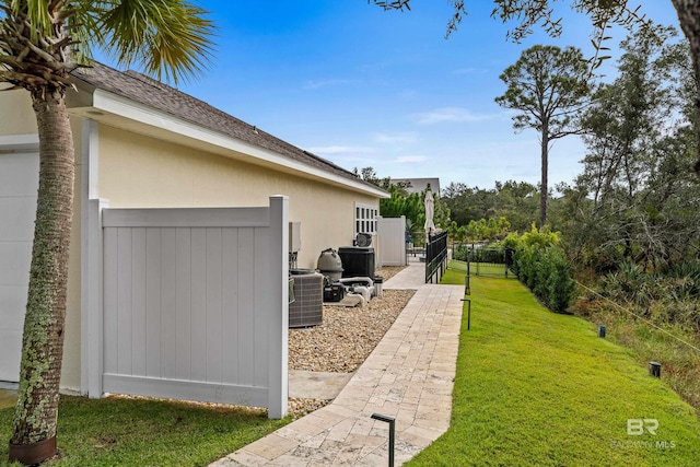 view of property exterior with roof with shingles, fence, central AC, and a yard